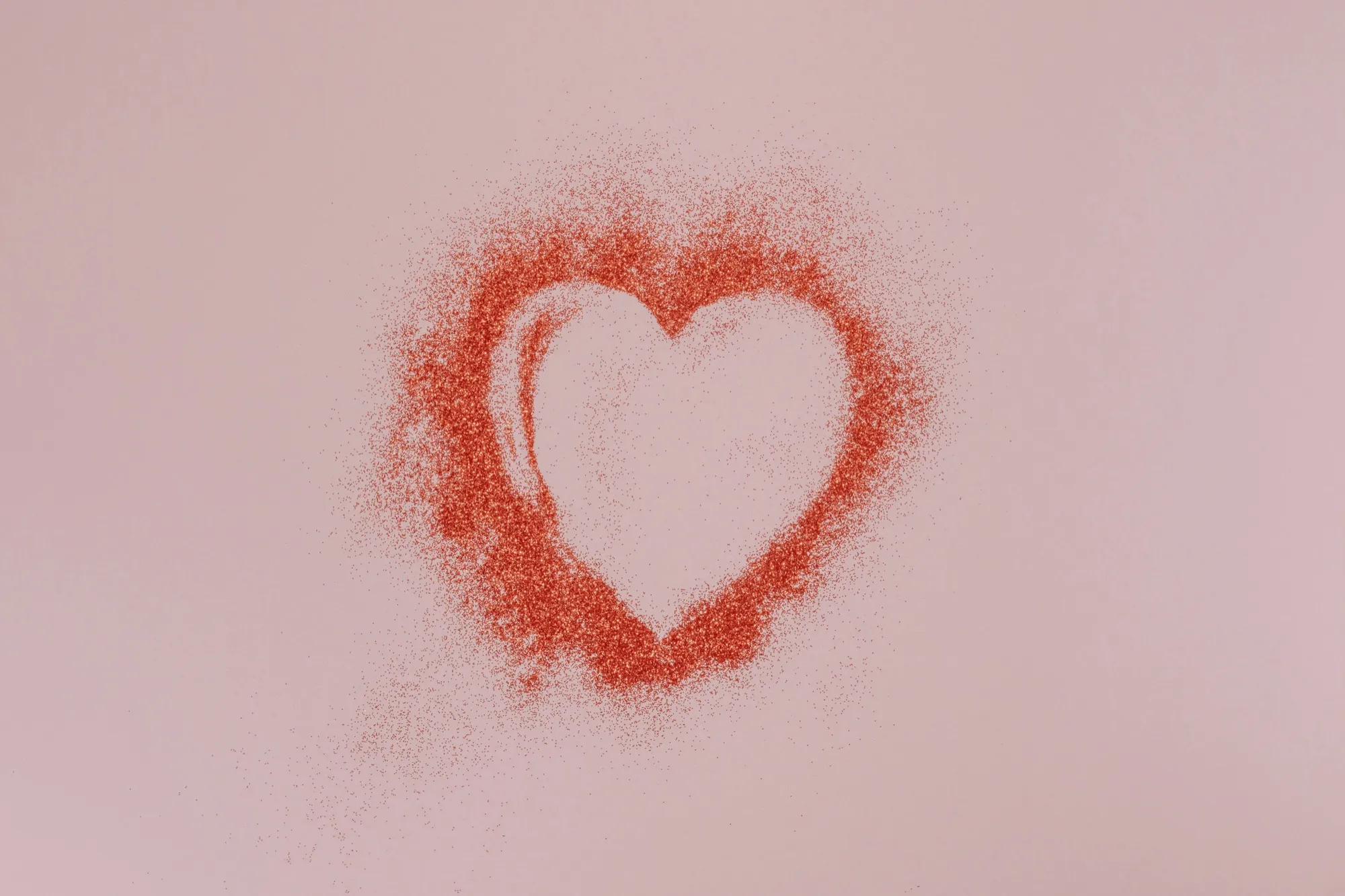 A heart traced in red sand or glitter on a soft pink background
