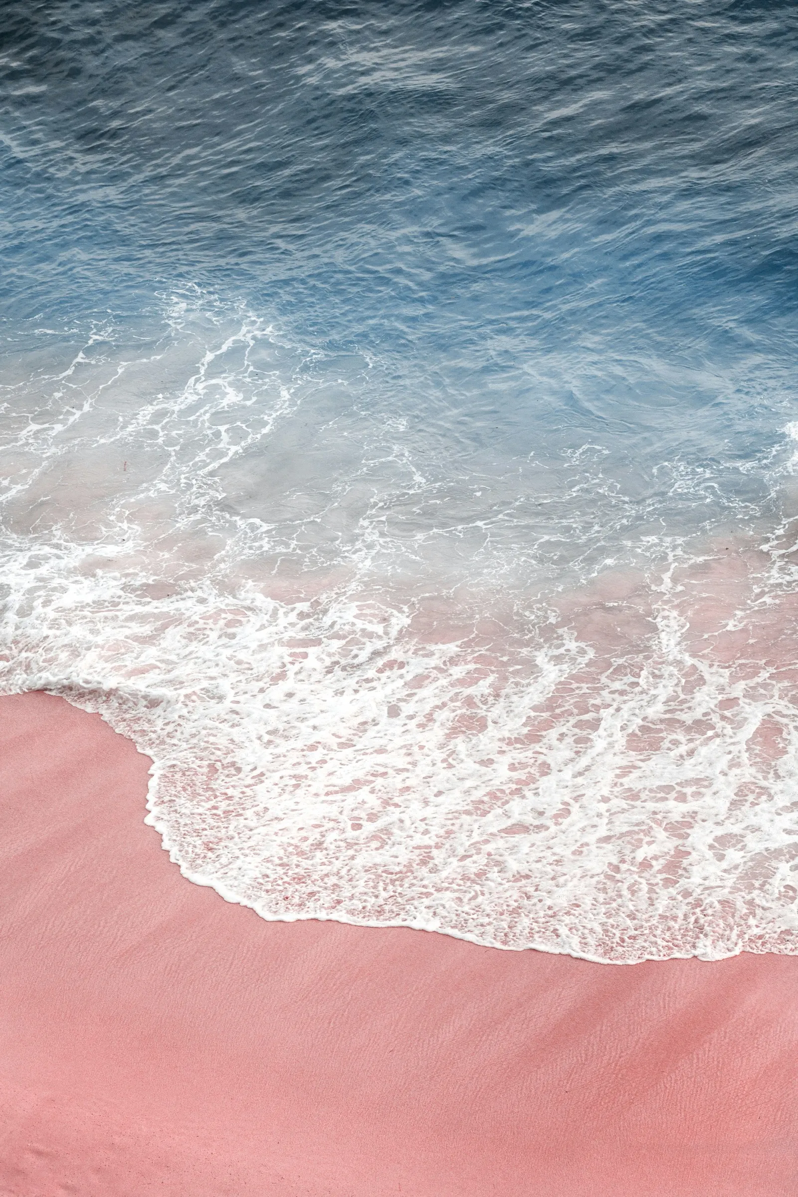 Aerial view of deep blue ocean water meeting pink sand at the shoreline