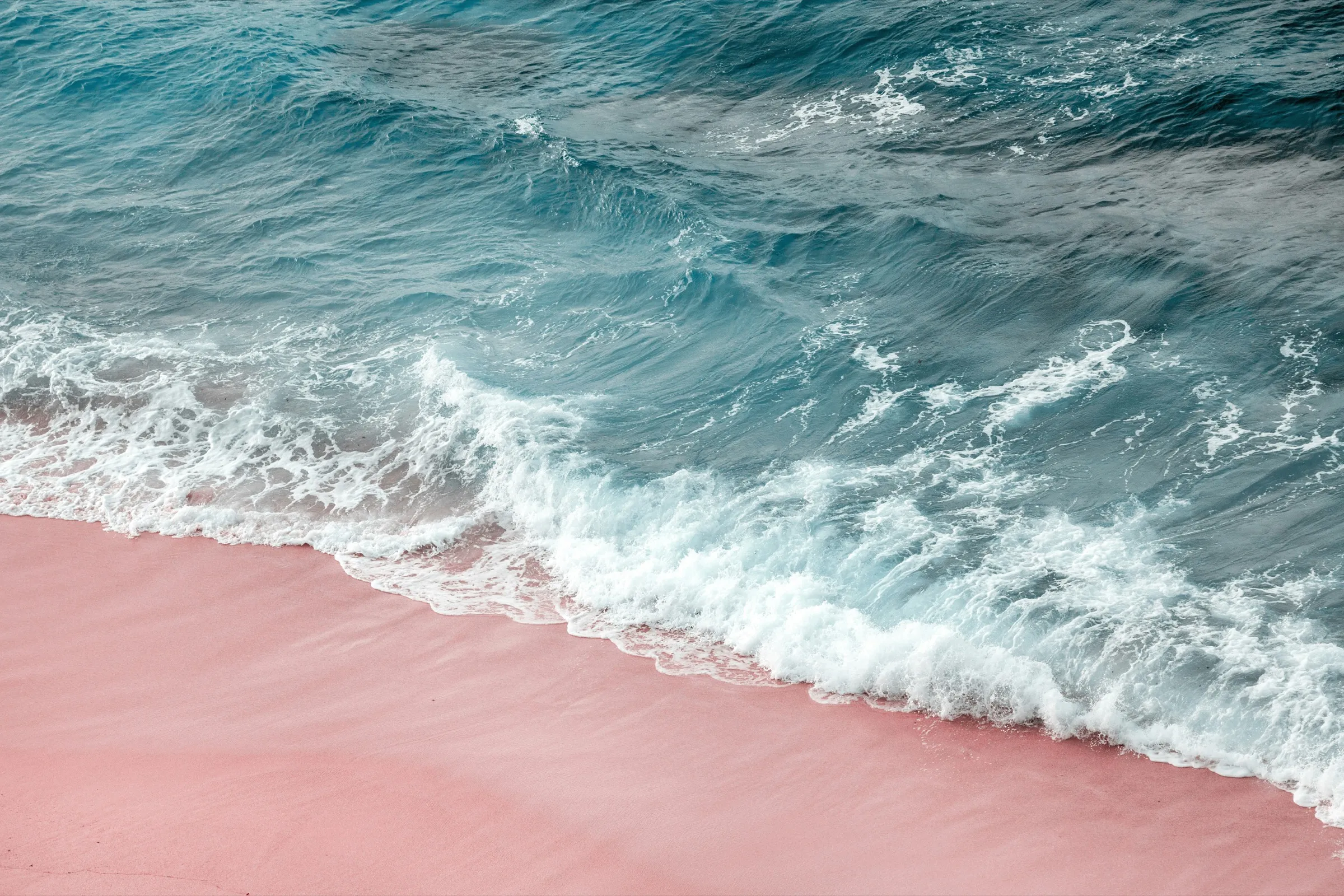 Aerial view of a turquoise wave breaking onto pink sand