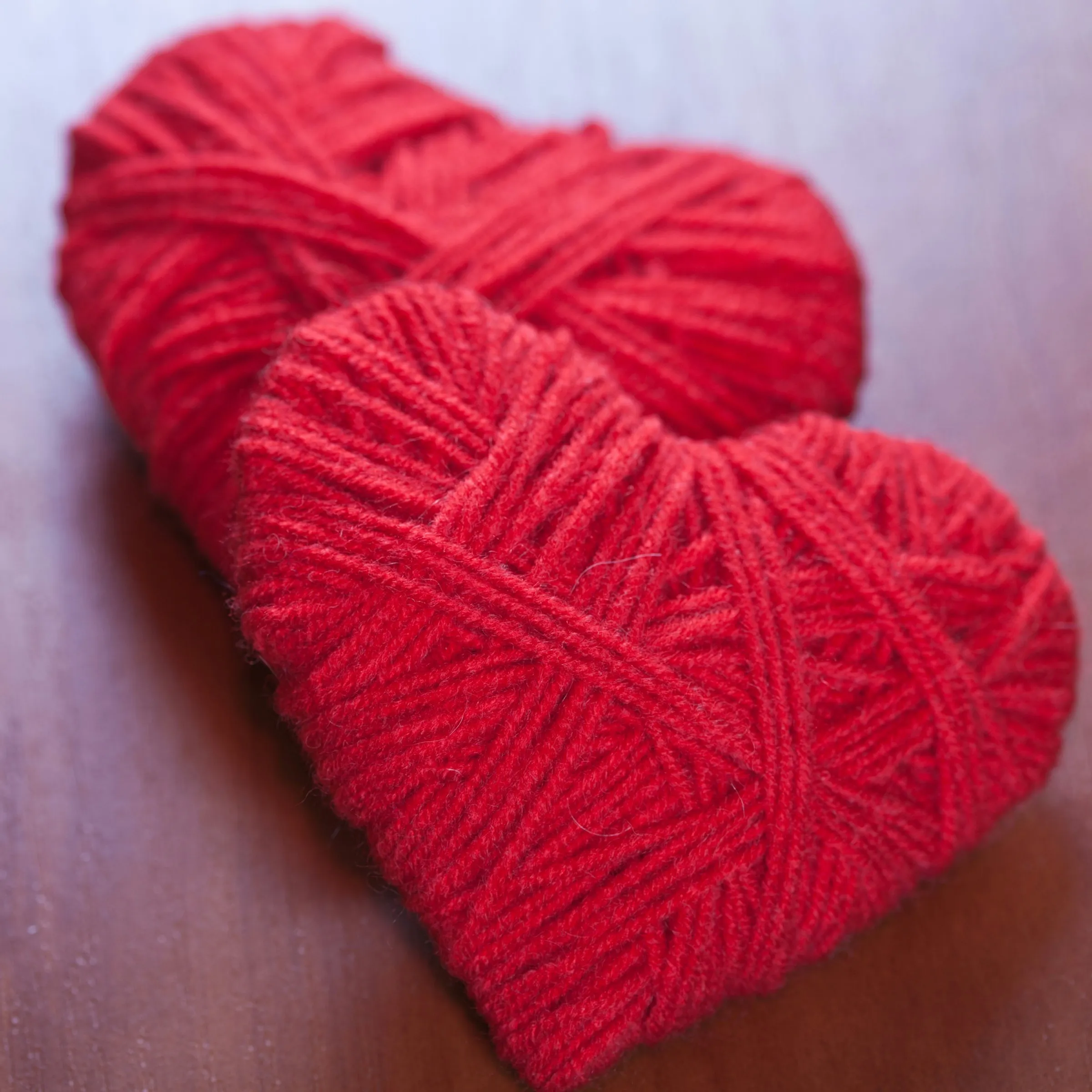 A stitched red felt heart resting on a bed of pink, red, and white pom-poms