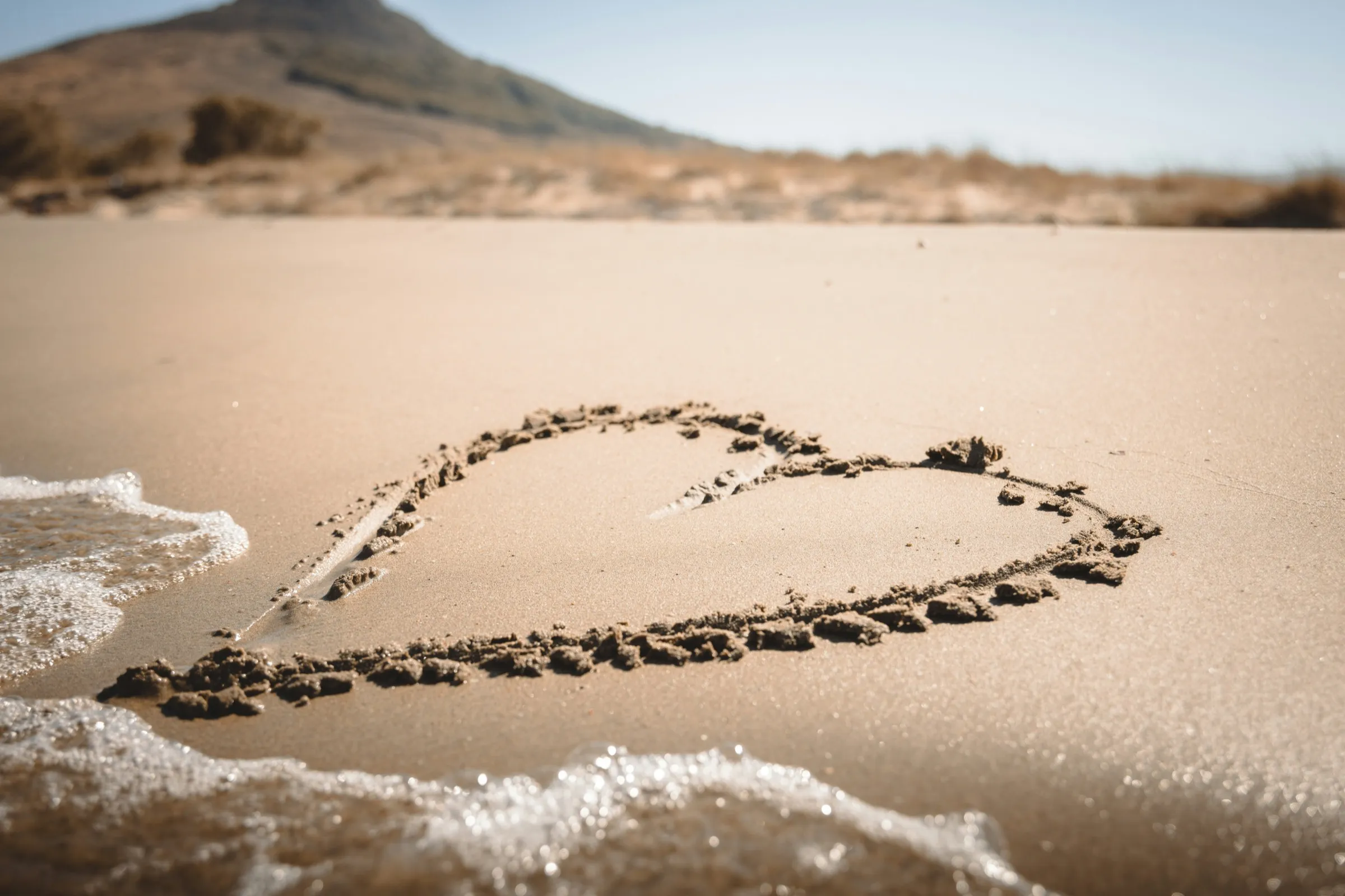 A heart drawn in beach sand, with a desert hillside in the background